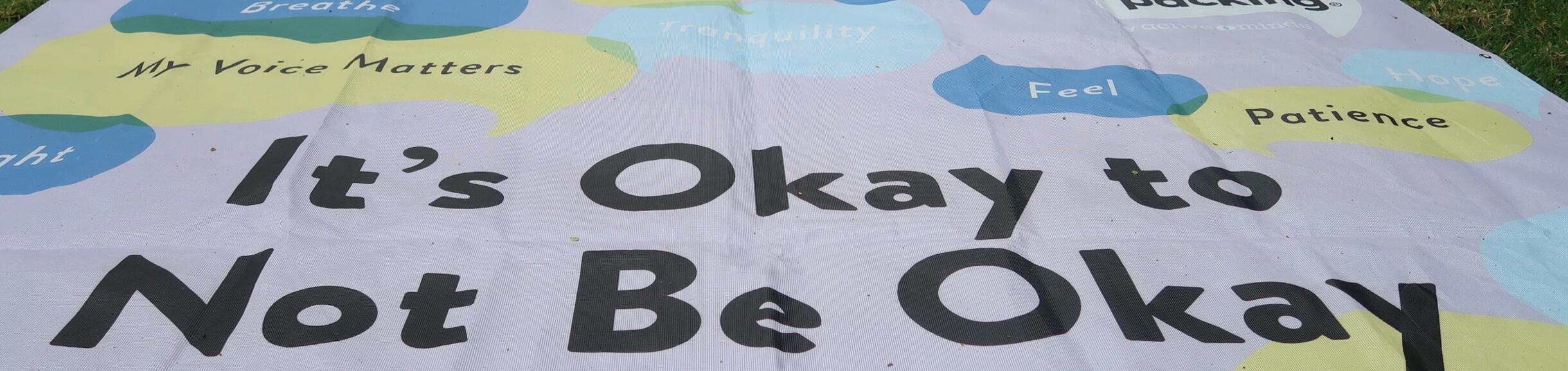 Banner laying on grass that states "It's okay to not be okay" 