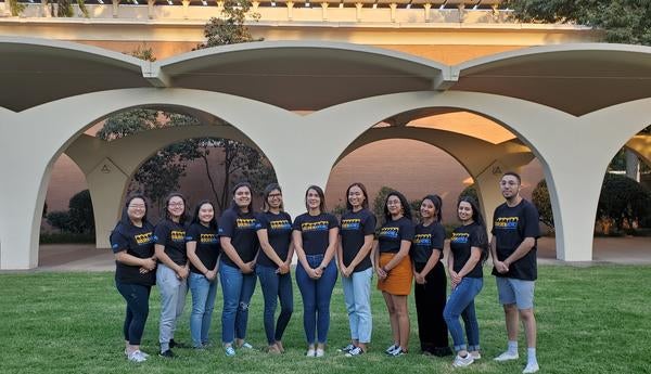 12 people with Golden ARCHES t-shirts standing in front of the Rivera Library arches, smiling and posing in a straight line